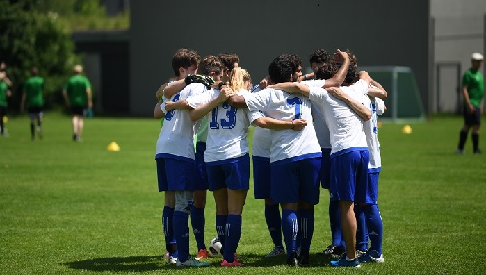 © Andreas Gebert Ein Gruppe Junger Menschen in Fußballtrikots steht in einem Kreis zusammen auf dem Fußballfeld.